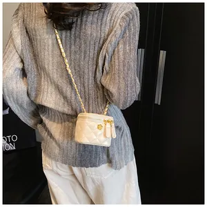 Close-up of beige quilted cylinder bag with gold camellia detail on leather chain