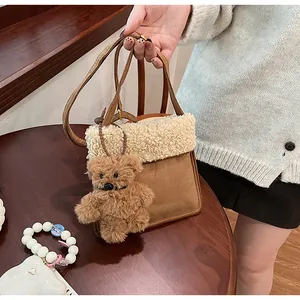 Detail of a brown suede crossbody bag featuring plush fleece trim and a small teddy bear charm