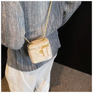Detail of cream mini crossbody bag featuring diamond quilting and gold camellia logo
