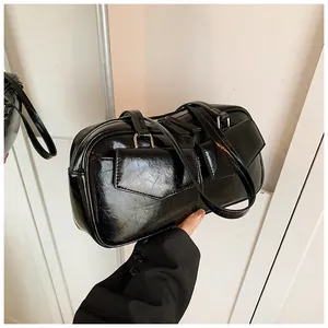 Detalle de bolso de hombro en cuero negro brillante con arrugas y dos bolsillos frontales