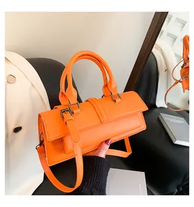 Detail einer orangefarbenen Lederhandtasche mit Schnallenriemen auf schwarzem Lederhocker