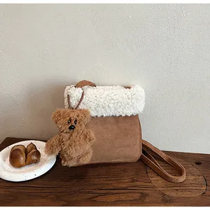 Detail of a brown suede shoulder bag featuring plush white wool trim and a cute bear charm