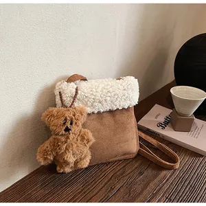 Close-up of suede shoulder bag with white fleece flap and a cute brown teddy bear charm