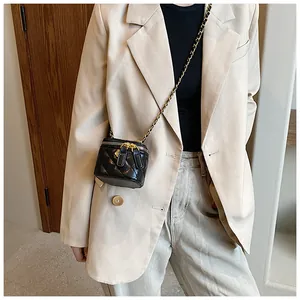 Detail of a mini black quilted crossbody bag with golden chain strap on a beige blazer