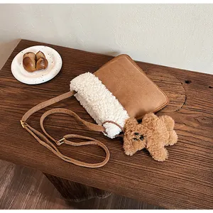 Close-up of brown suede and white fleece crossbody bag with a cute bear charm on a wood bench