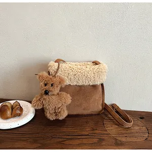 Close-up of brown suede crossbody bag with sherpa fleece trim and a plush bear charm