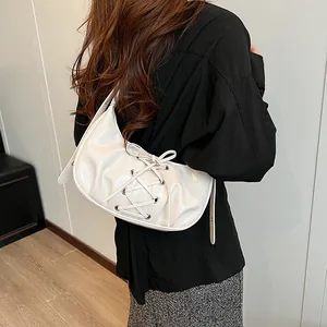 Detail view of cream white patent leather hobo bag featuring lace-up straps and metal eyelets