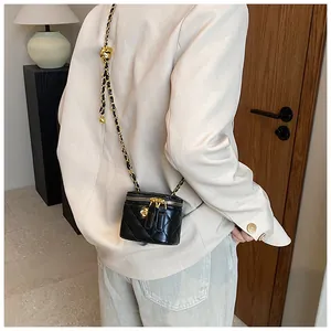 Close-up of a mini quilted black crossbody bag with golden chain and floral charm