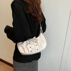 Detail view of cream-colored crescent bag with ribbon laces and glossy finish on model