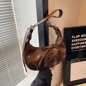 Detail of corset-style lacing on a brown patent leather half-moon shoulder bag