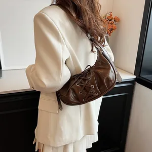 Detail of dark brown glossy patent leather half-moon bag with lace-up ribbon design