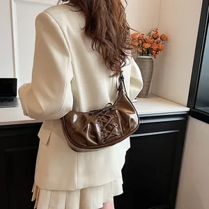 Detail of dark brown glossy underarm bag with lace-up ribbon design and metal eyelets