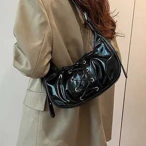Glossy black crescent shoulder bag with lace-up details and silver eyelets on women model
