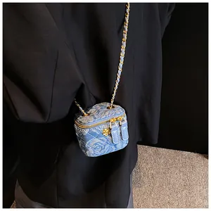Close-up of a mini quilted blue denim crossbody bag with gold chain and floral detail