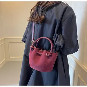 Close-up of burgundy suede bucket bag with knotted handle and slim shoulder strap