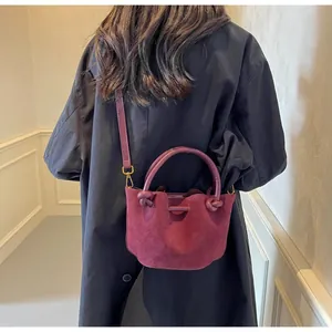 Detail of burgundy suede bucket bag showing a unique knotted handle and shoulder strap