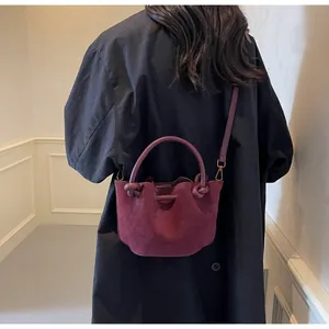 Detail view of burgundy suede bucket bag featuring knotted handle and gold-tone hardware