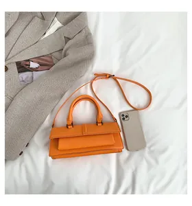 Flache Liegeansicht einer orangen Lederhandtasche mit Trageriemen im Lifestyle-Stil