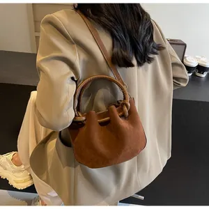 Detail view of brown faux suede bucket bag with round handles and drawstring closure