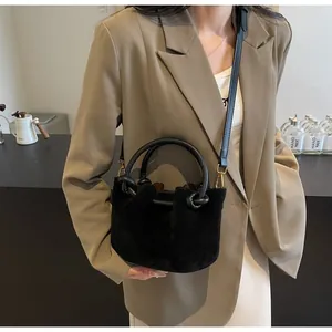 Detail of a black suede bucket bag styled with a khaki blazer in a modern setting