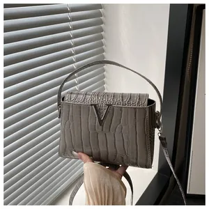Detail of grey crocodile embossed leather handbag with silver metal V-logo buckle