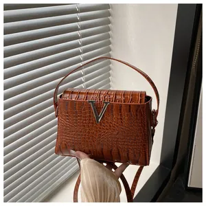 Detail of brown crocodile pattern handbag with silver V-shaped buckle and leather texture