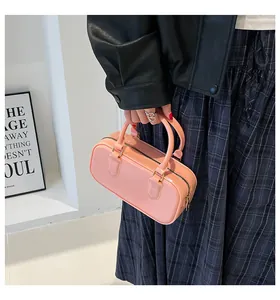 Detail of a bright pink cylindrical handbag featuring glossy patent leather and sturdy handles