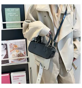 Detail showing the glossy black patent leather finish and round handles of the shoulder bag