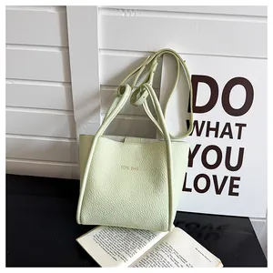 Detailansicht der pistaziengrünen Ledertasche mit Goldaufdruck auf einem eleganten Ständer