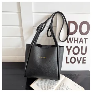 Detail der schwarzen Tote-Bag aus genarbtem Leder mit goldener Aufschrift und Trageriemen