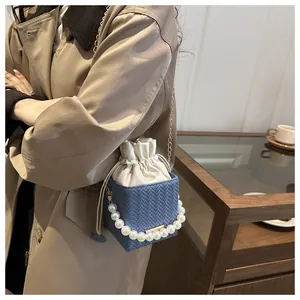 Blue woven bucket bag featuring pearl handle and gold chain strap shown on a table