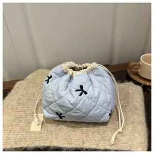 Detailed close-up of quilted light blue drawstring bucket bag with black bow embroidery