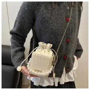 Detail of cream woven bucket bag featuring pearl handle and gold chain shoulder strap