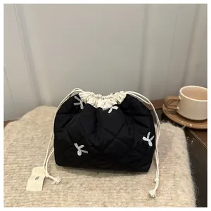 Detail of black quilted tote bag with floral embroidery and cream drawstring closure