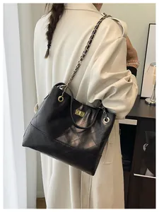 Close-up of black quilted leather tote bag with gold chain strap on beige coat
