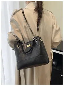 Detail of black quilted leather chain bag with gold lock worn with a beige trench coat