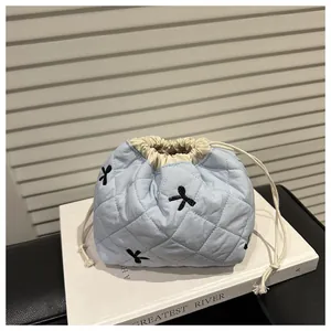 Detail of light blue quilted drawstring bag with black bow embroidery and rhombus texture