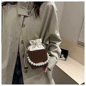 Close-up of woven bucket bag featuring pearl handle and gold chain strap detail