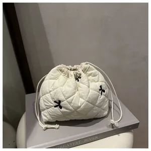 Detailed shot of a beige quilted drawstring makeup bag featuring black bow embroidery