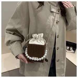 Detail of square bucket bag showing pearl handle, metal chain, and woven PU leather texture