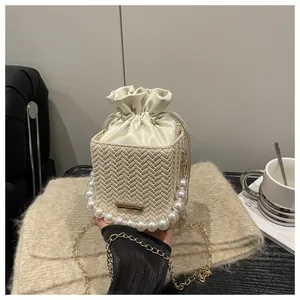 Detail of cream woven bucket bag with pearl handle, gold chain and drawstring inner pouch