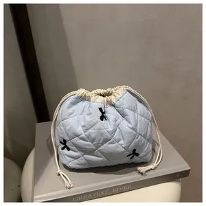 Detailed view of light blue quilted cosmetic bag with black bow embroidery and drawstring
