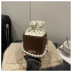 Detailed close-up of woven bucket bag with pearl handle and golden chain strap