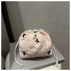 Detail of pink quilted drawstring makeup bag with black bow embroidery on a minimalist setup