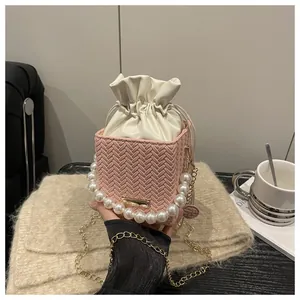 Detail of pink woven bucket bag featuring large pearl handle and gold chain strap