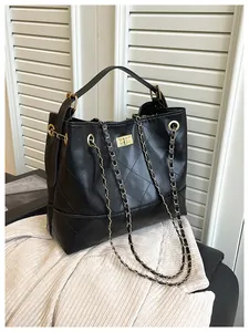 Detail of black quilted leather tote with gold twist lock and chain strap on fabric