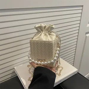 Creamy white woven bucket bag with elegant pearl handle and gold chain shoulder strap