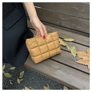 Gesteppte senfgelbe Nylon-Clutch von Model gehalten in einer herbstlichen Parkumgebung