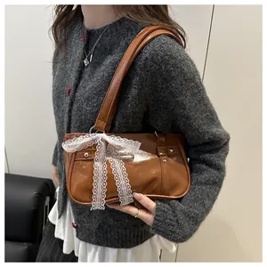 Close-up of brown patent leather underarm bag with white lace bow detail on a grey sweater