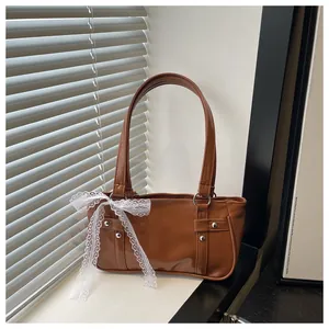 Detail of dark brown leather underarm bag with white lace bow and silver rivets